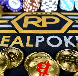Stacks of poker chips in various colors are arranged in the background, while in the foreground, there are numerous golden coins featuring the Bitcoin symbol. The text 'REALPOKER' is prominently displayed in gold and silver lettering on a dark background.